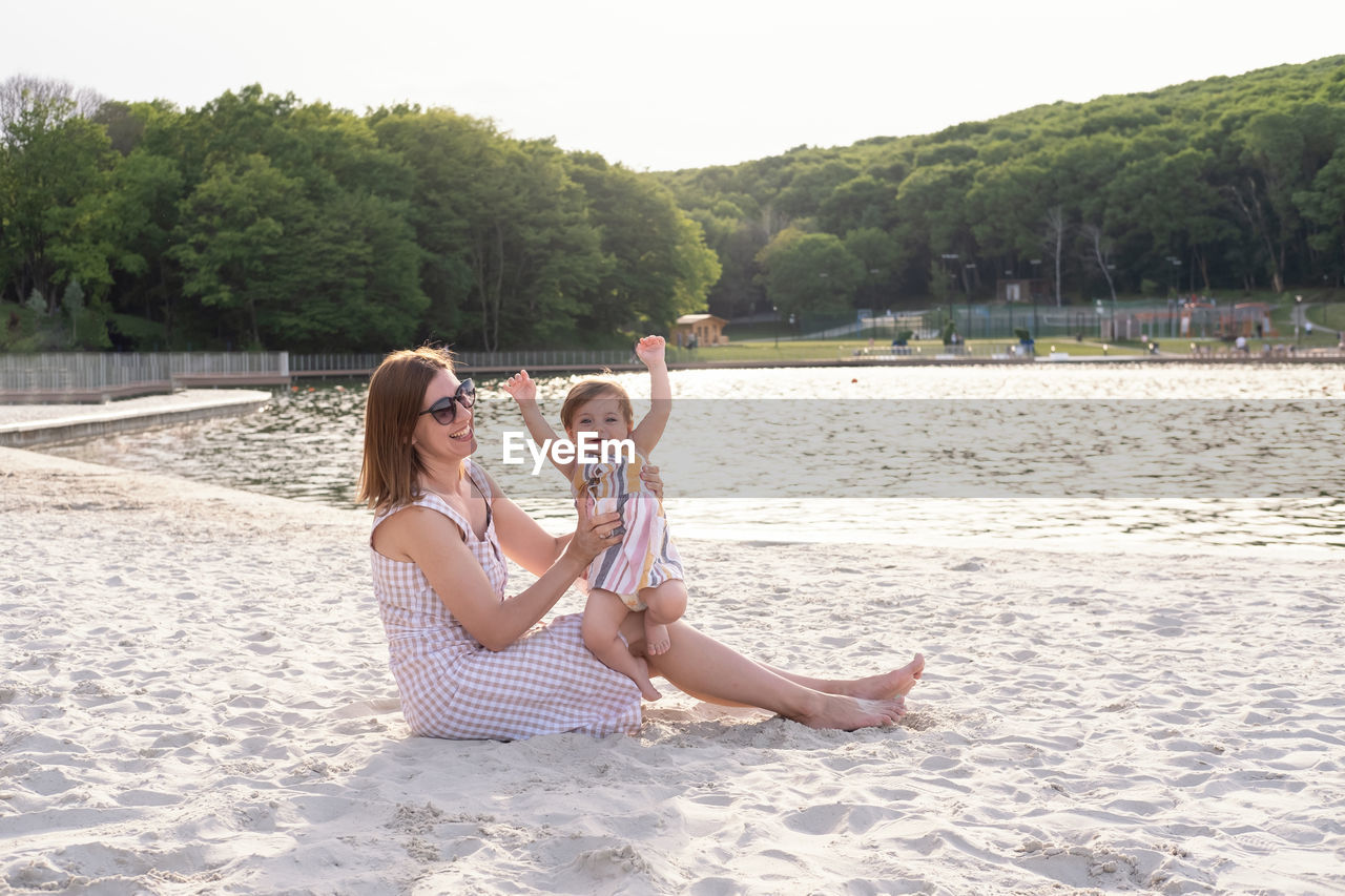 portrait of young woman drinking water while sitting at beach