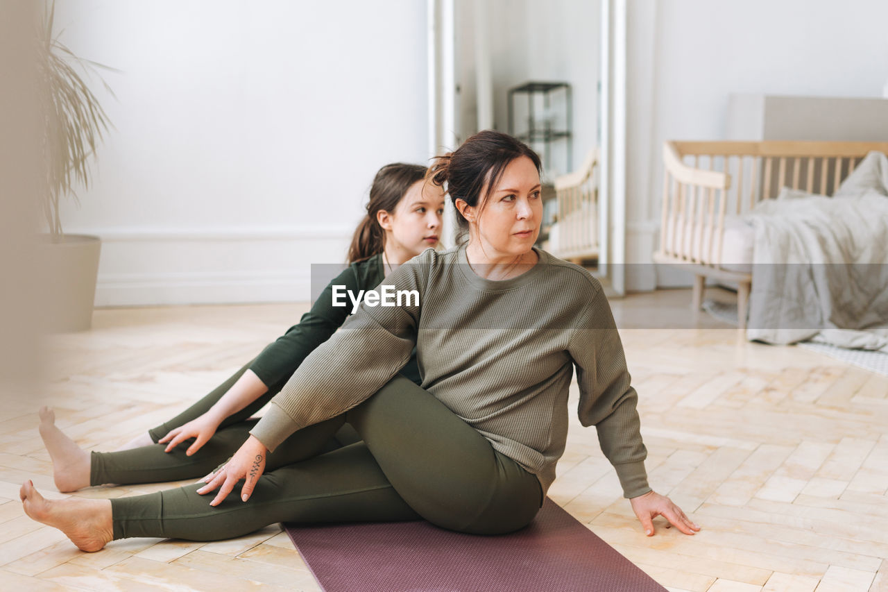 Attractive mother middle age woman and daughter teenager ptactice yoga together in the bright room