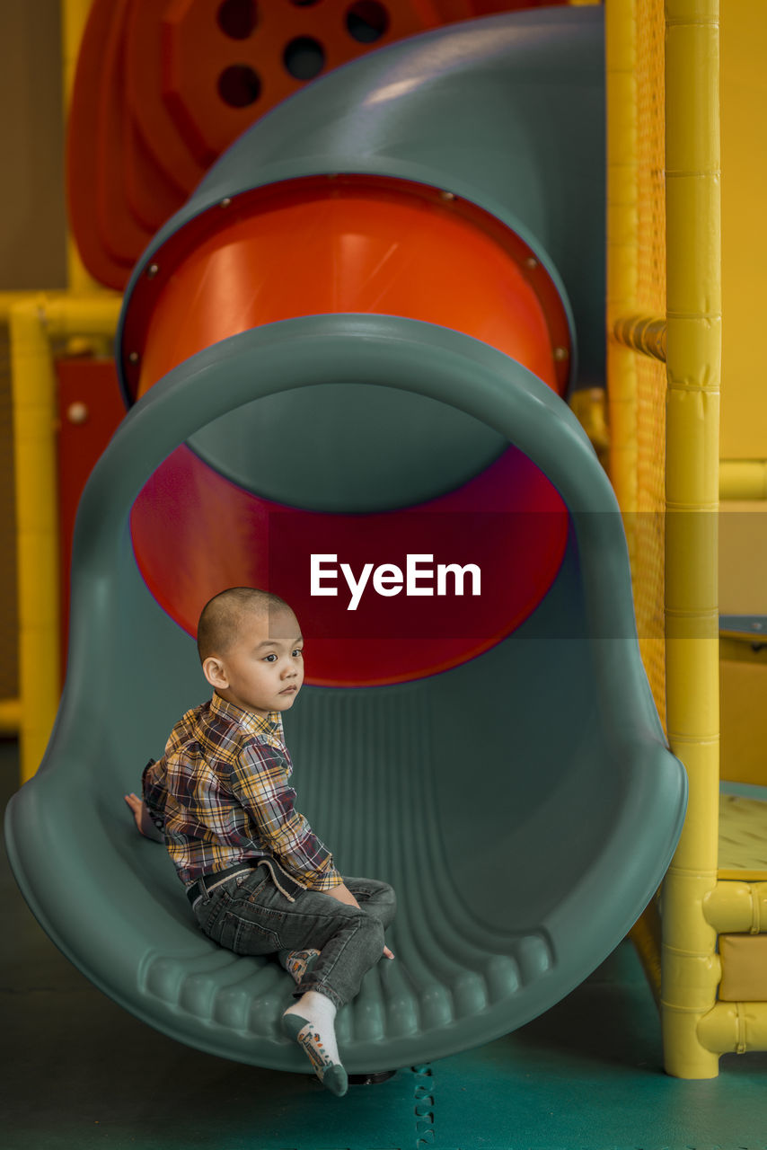 Side view of cute boy looking away while sitting on slide