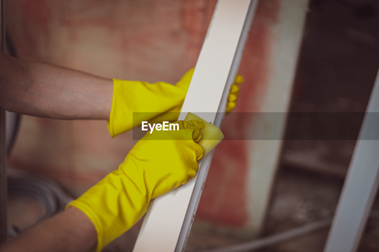 Hands of a young caucasian man in yellow rubber gloves washes window frames with a sponge and soap