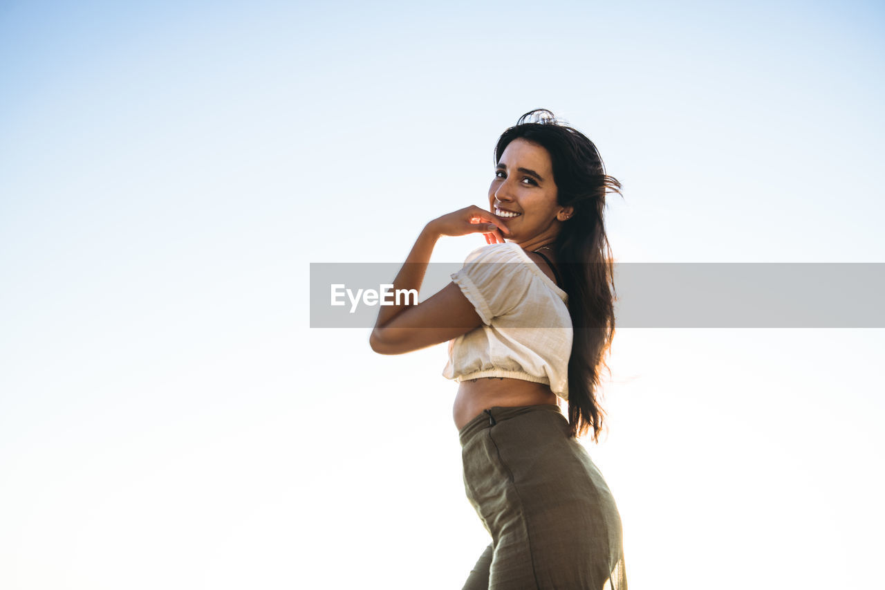 Young latina woman smiling by the ocean at golden hour in summertime