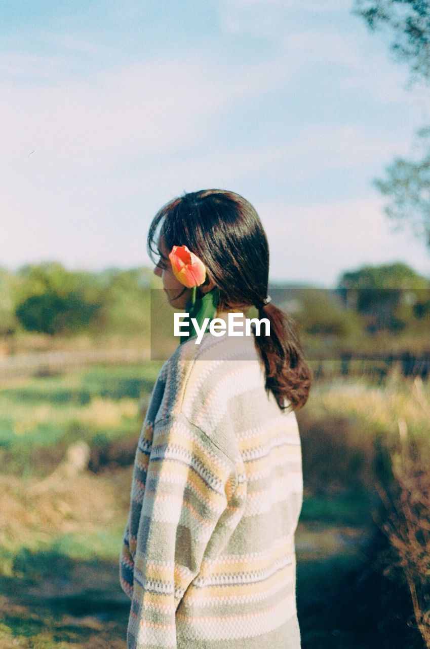 REAR VIEW OF YOUNG WOMAN STANDING ON FIELD