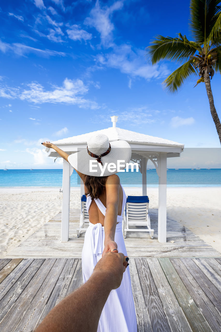 rear view of woman with arms outstretched on beach against sky