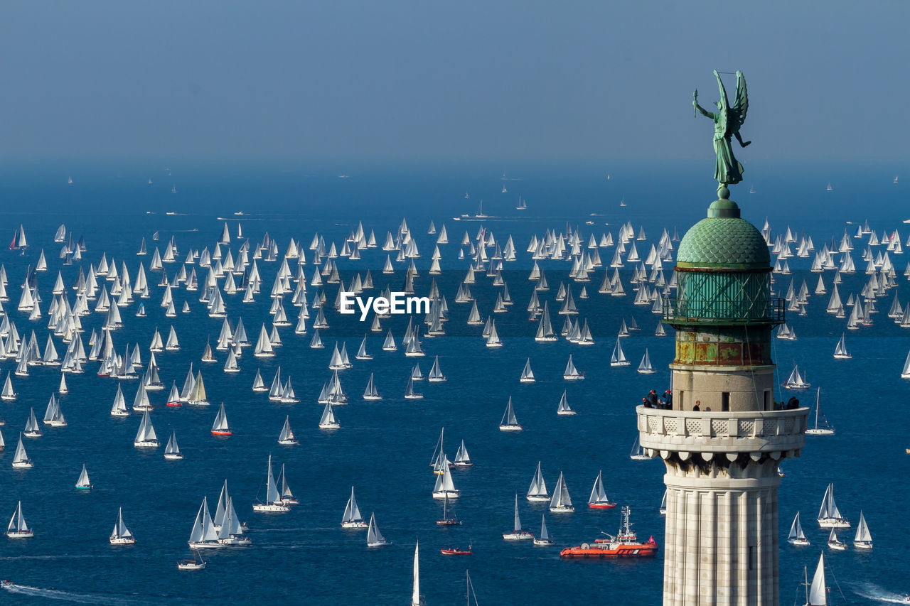 Lighthouse with statue against ships in sea 