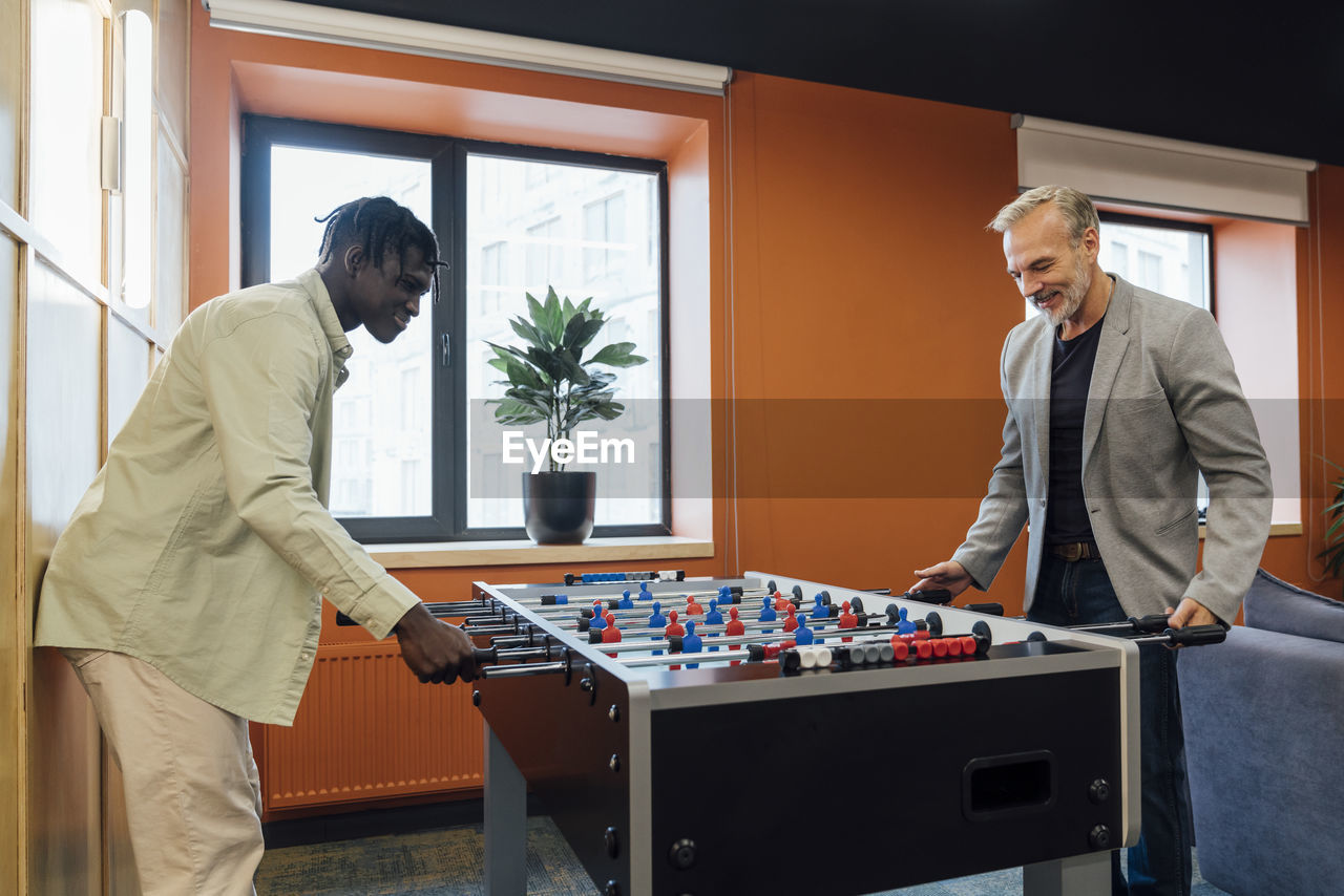 Smiling businessman playing foosball with colleague in office