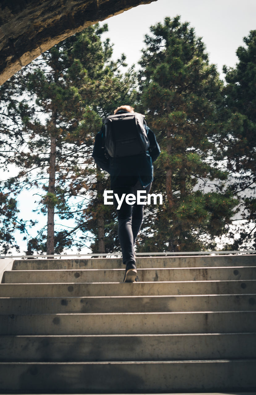 Low angle view of hiker with backpack moving up on steps at forest