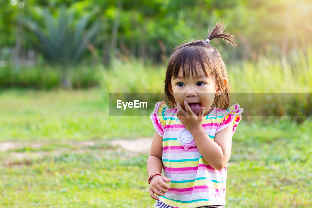 Cute baby girl with mouth open standing on land