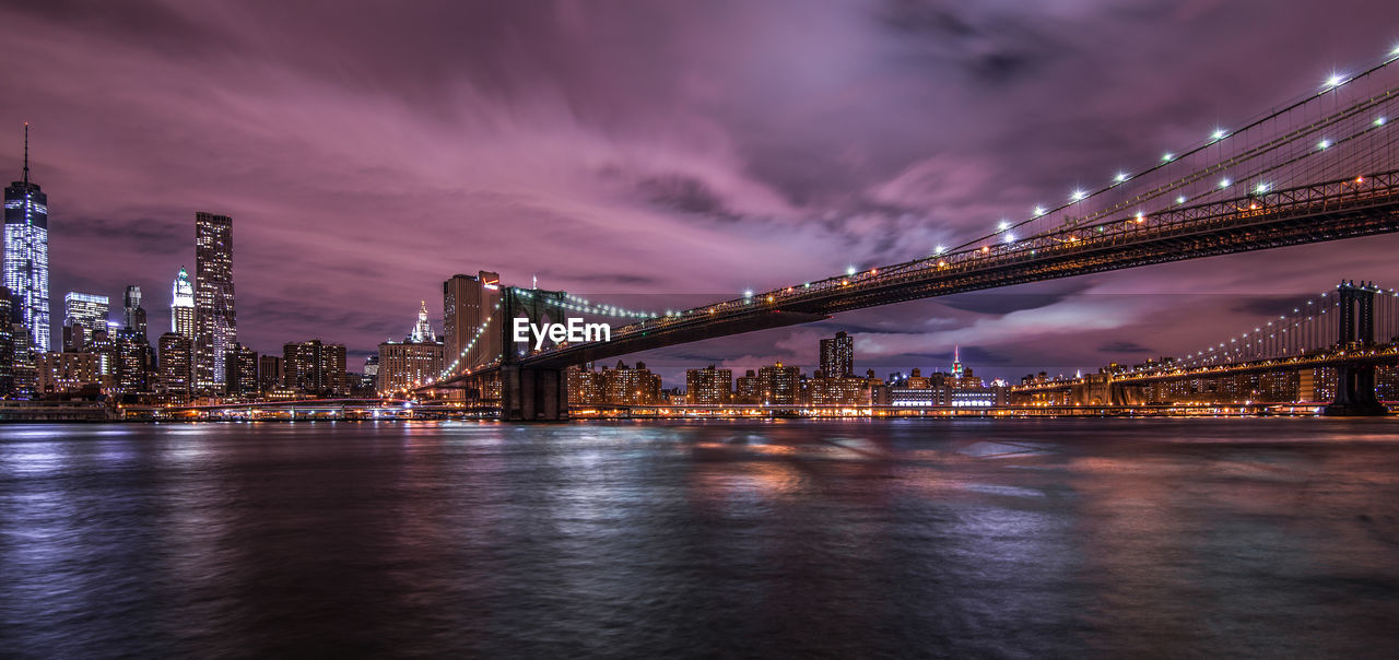 Illuminated bridge over river with city in background