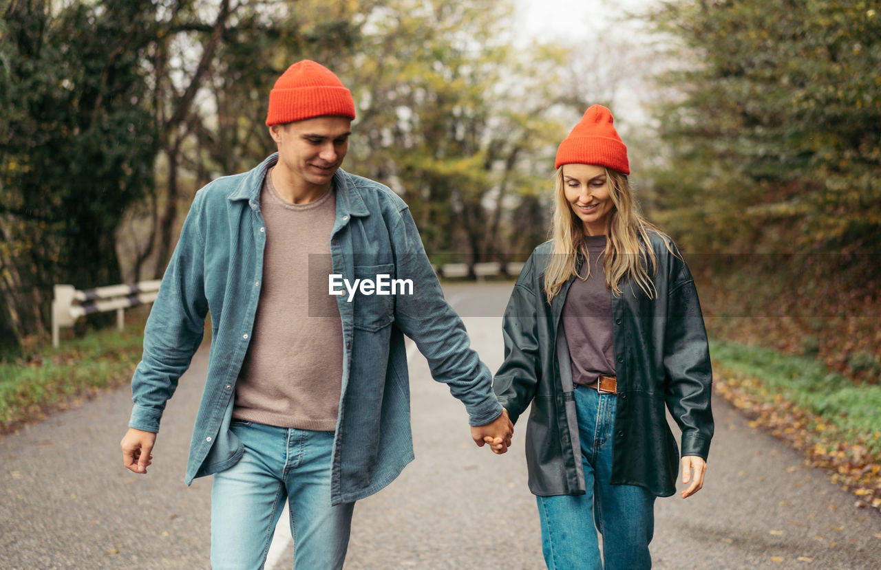 A man and a woman in love walk along the road holding hands.