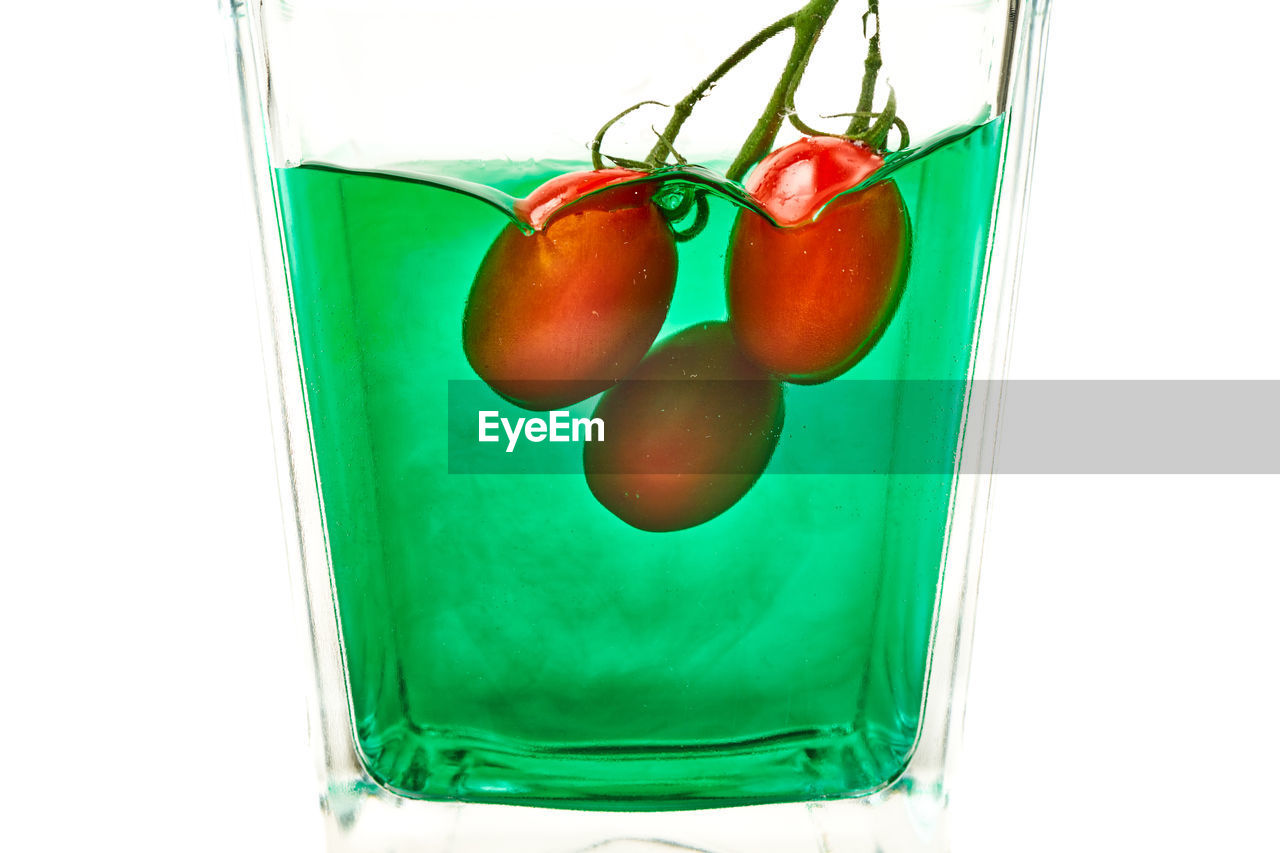 Close-up of fresh cherry tomatoes in glass with green liquid over white background