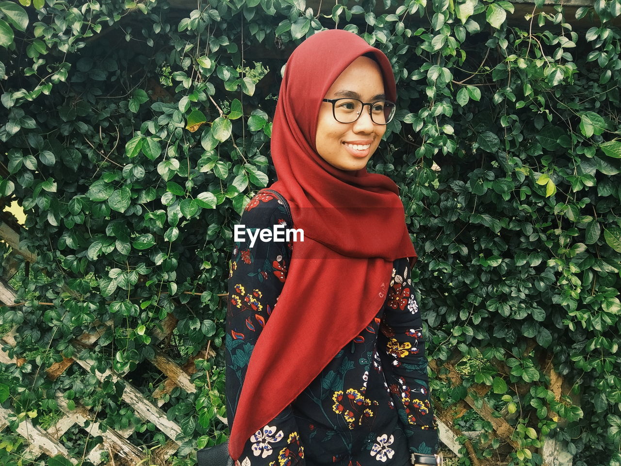 Smiling young woman wearing hijab looking away while standing against plants in park