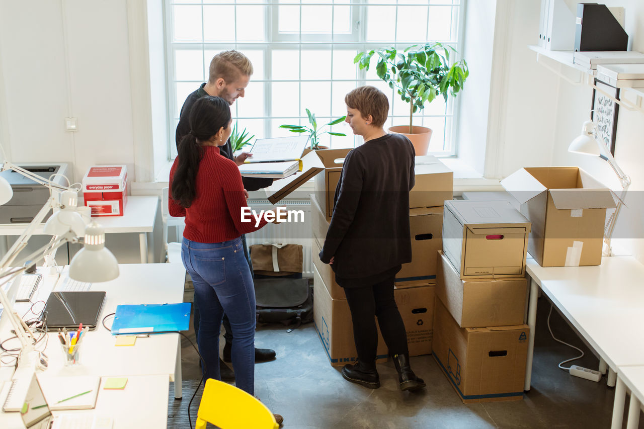 High angle view of business colleagues discussing over documents by cardboard boxes at office