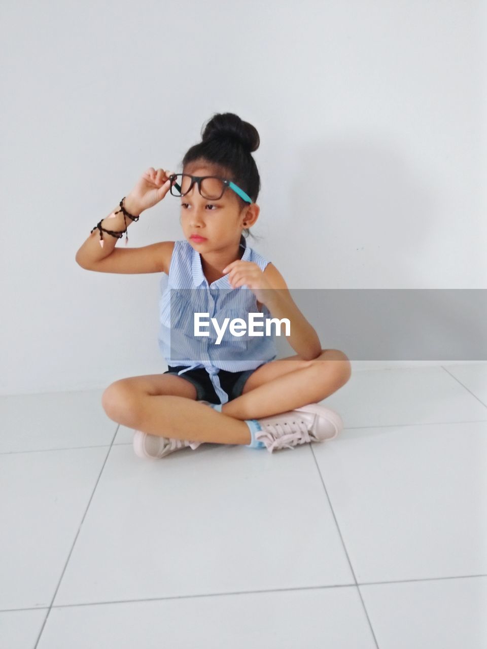 Thoughtful girl wearing eyeglasses while sitting on tiled floor