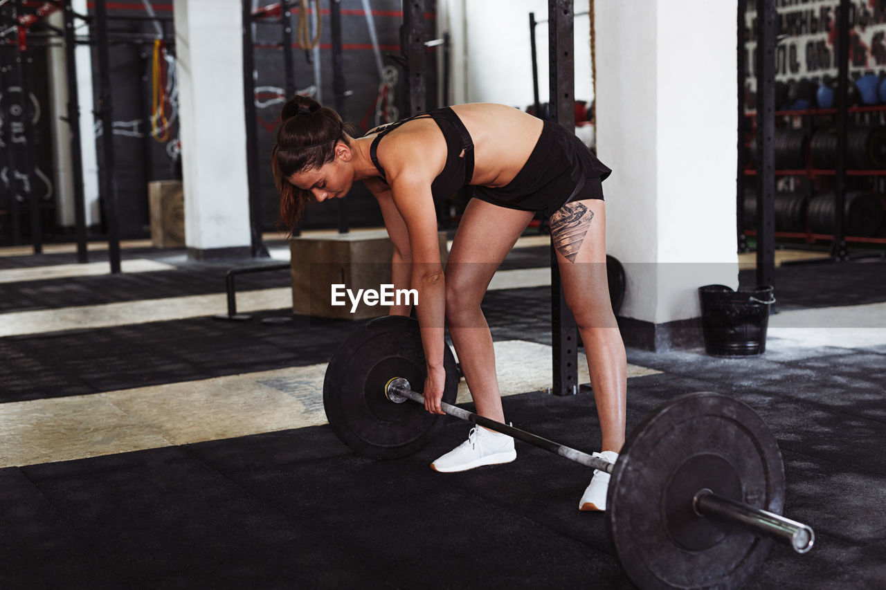 Full length of young woman lifting barbell at gym