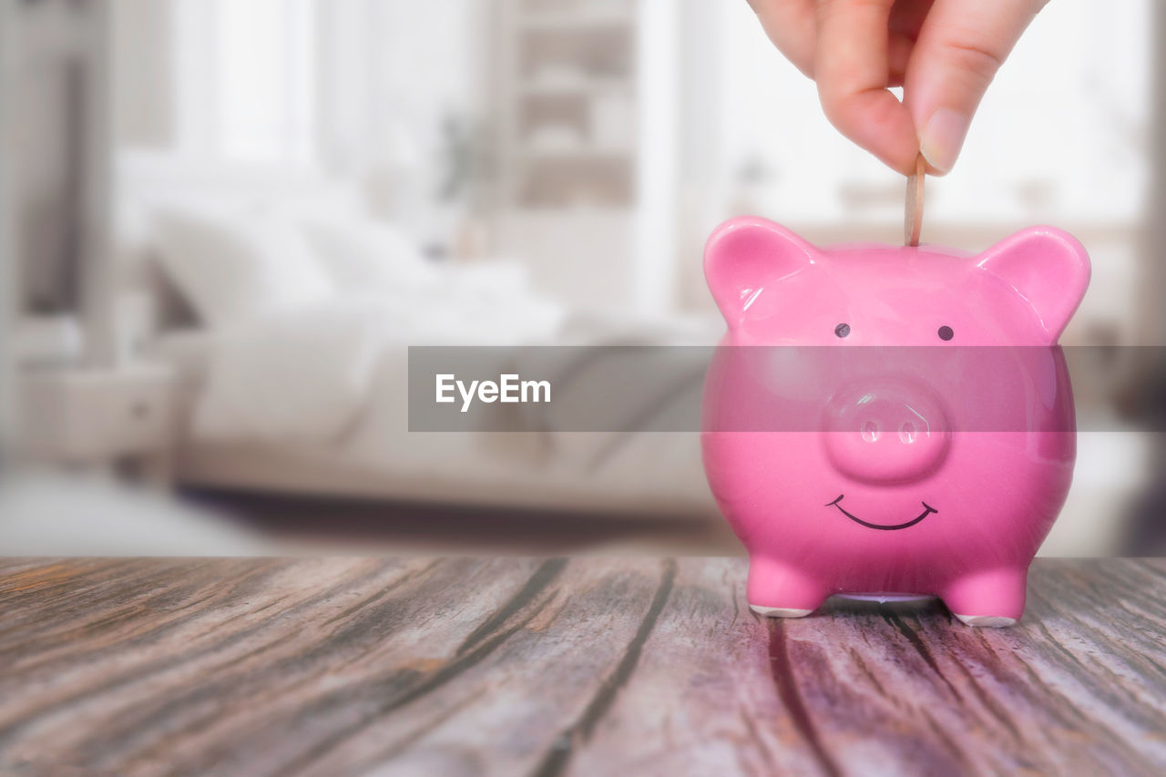 cropped hand of man putting coin in piggy bank on table