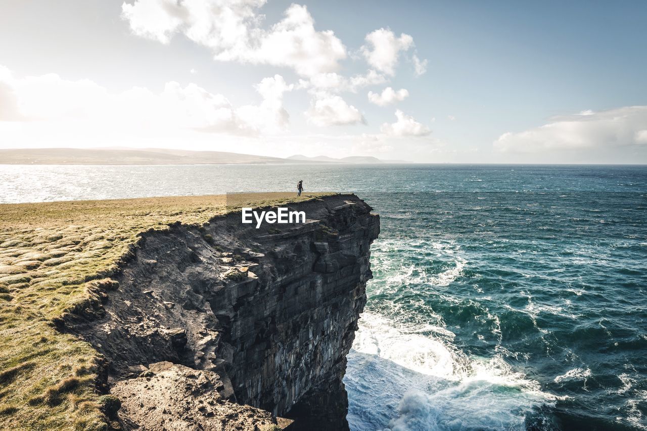 Silhouette of man on rock by sea against sky