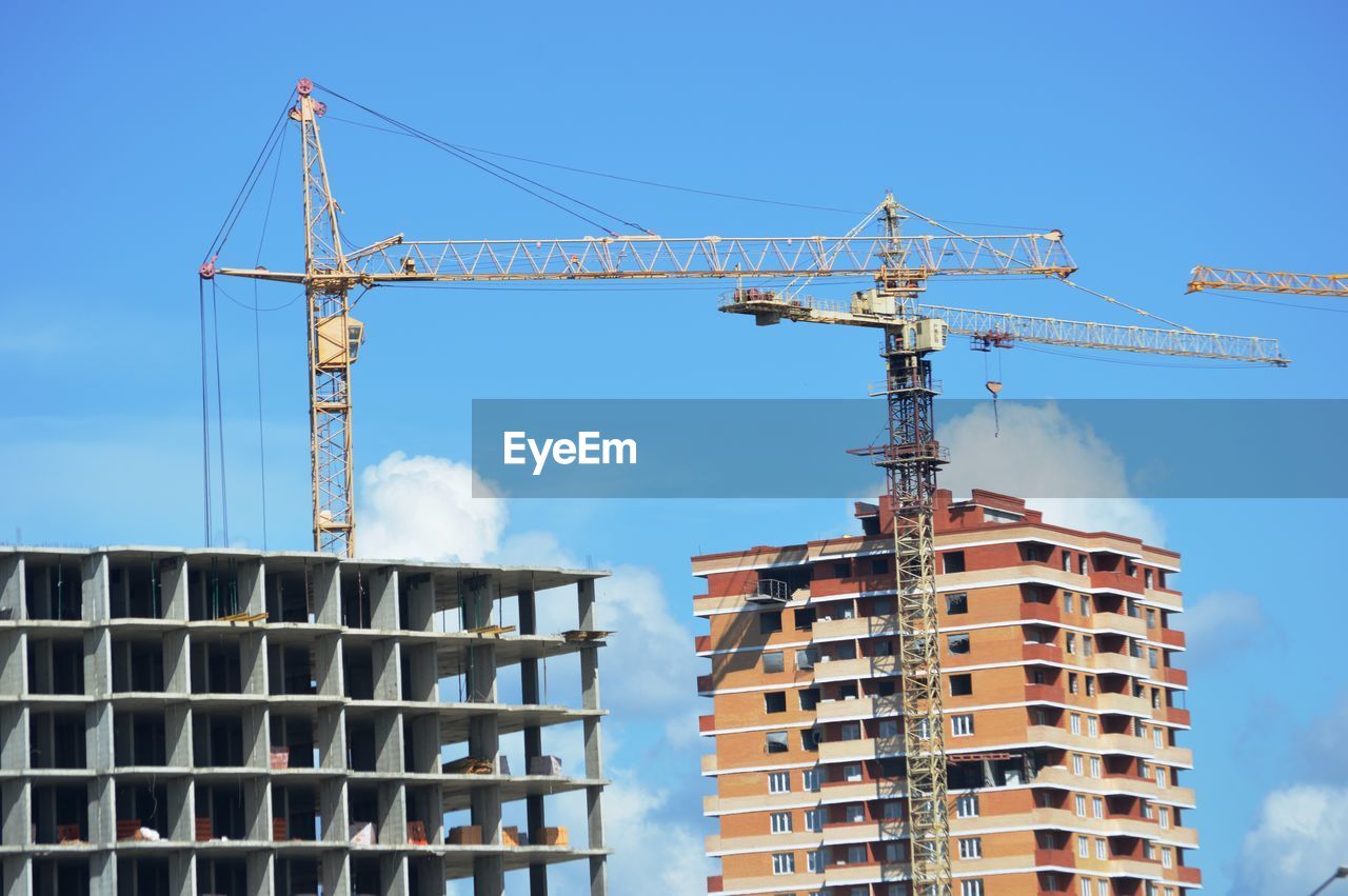 Low angle view of crane by building against sky