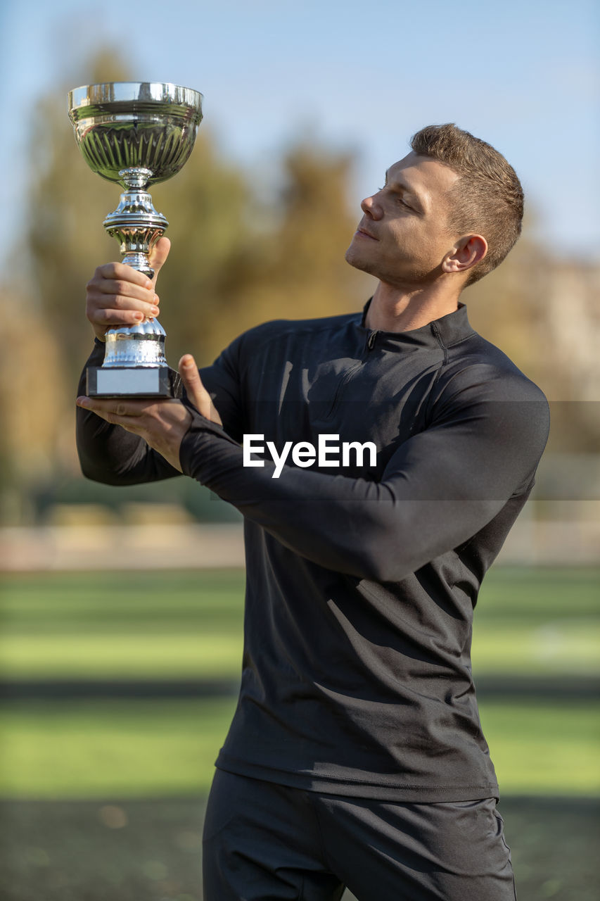 side view of man holding trophy against sky during sunset