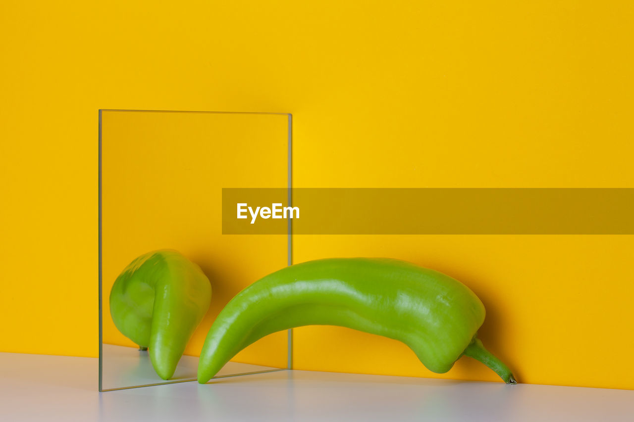 Green pepper is reflected in a mirror on a yellow background