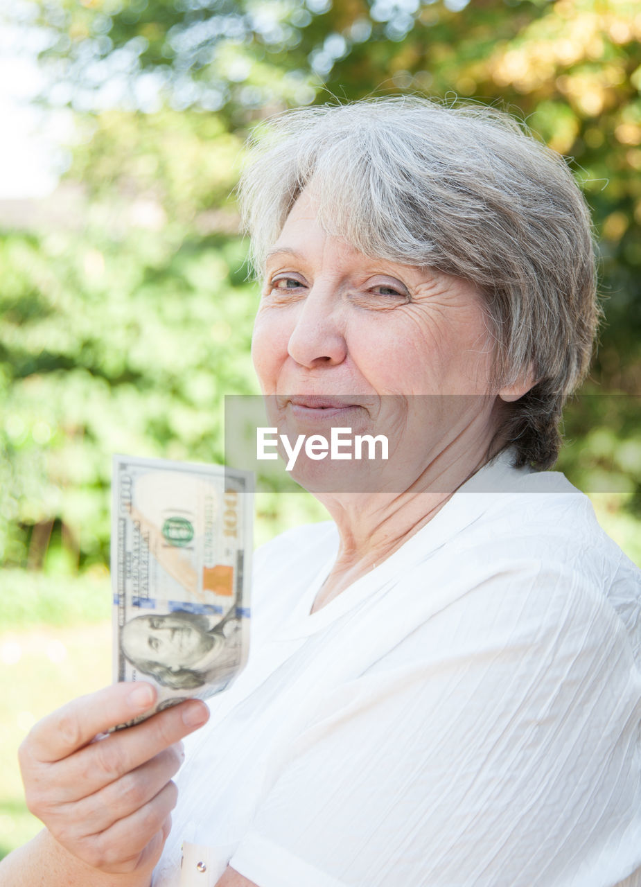 Smiling senior woman holding american one hundred dollar bill