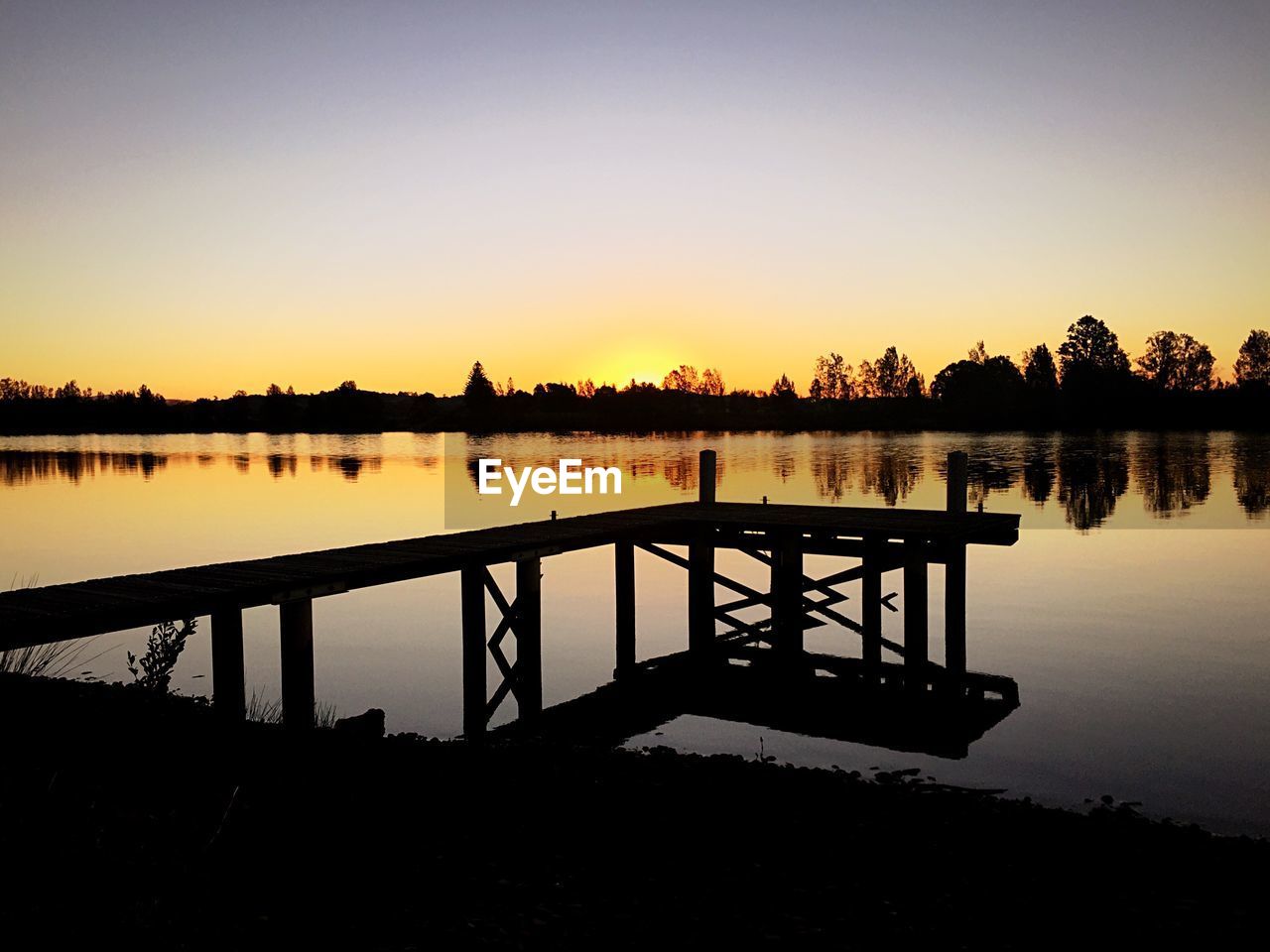 SILHOUETTE PIER IN FRONT OF CALM LAKE AGAINST CLEAR SKY