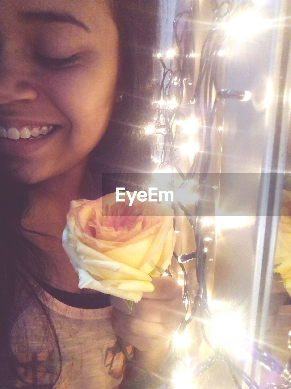 CLOSE-UP OF SMILING WOMAN WITH ILLUMINATED FLOWER IN BACKGROUND