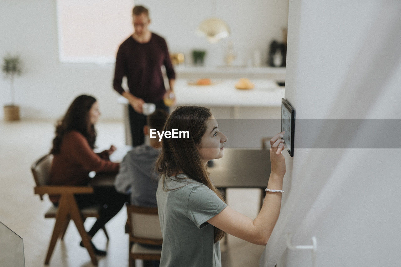 Pre-adolescent girl using digital tablet mounted on wall by family at modern home