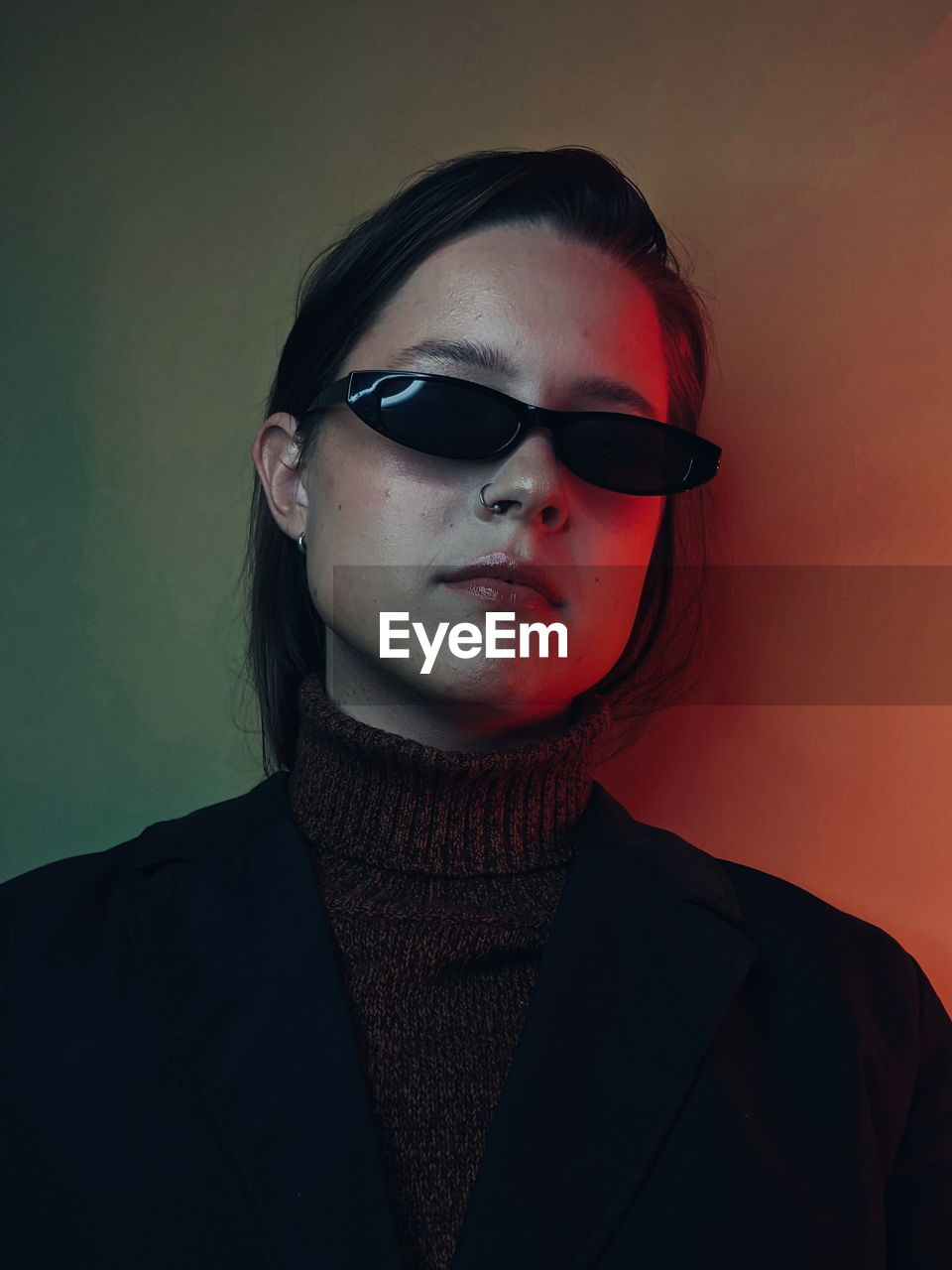 Portrait of young woman wearing sunglasses against wall