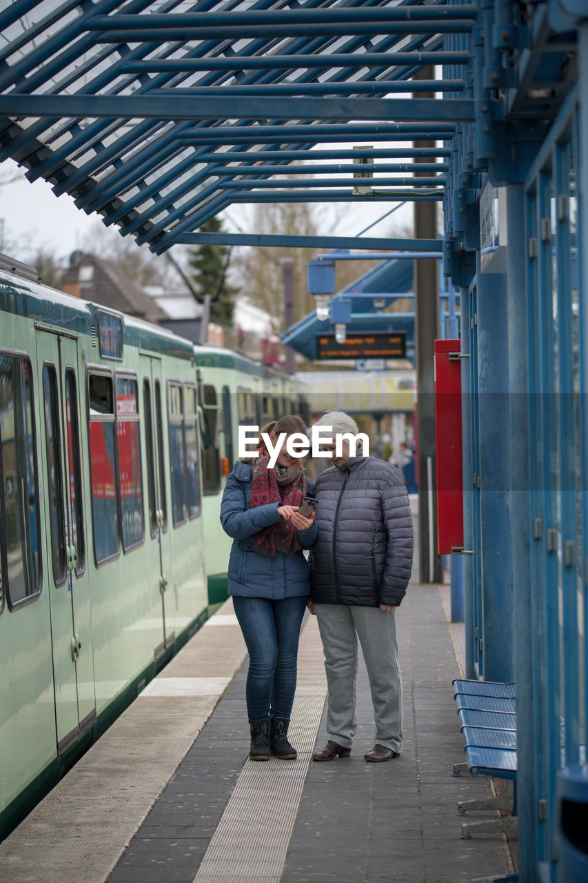 Grandmother and granddaughter using mobile phone at railroad station platform