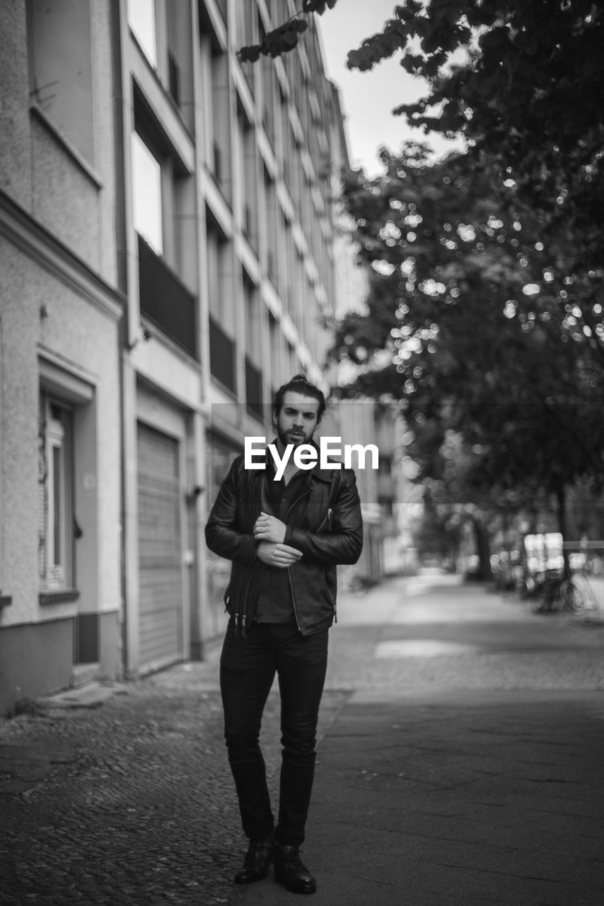 FULL LENGTH PORTRAIT OF YOUNG MAN STANDING AGAINST CITY