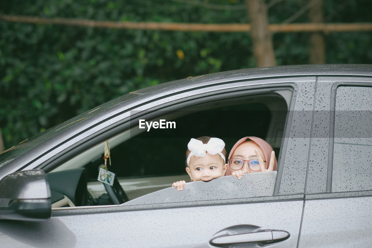 A young woman and his baby girl peeking outside car window