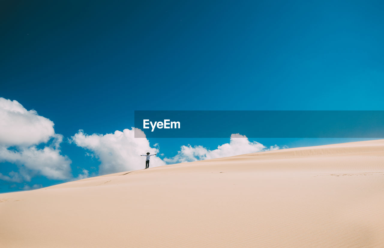 Low angle view of standing on sand dune at desert against blue sky