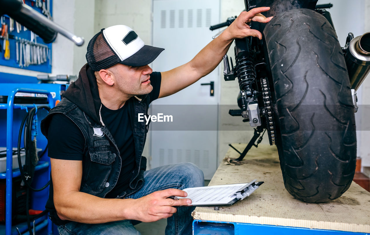 Side view of mature mechanic examining motorcycle in garage