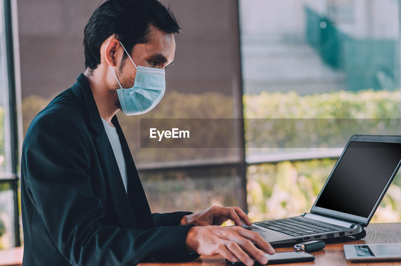 Man wearing mask using laptop at table