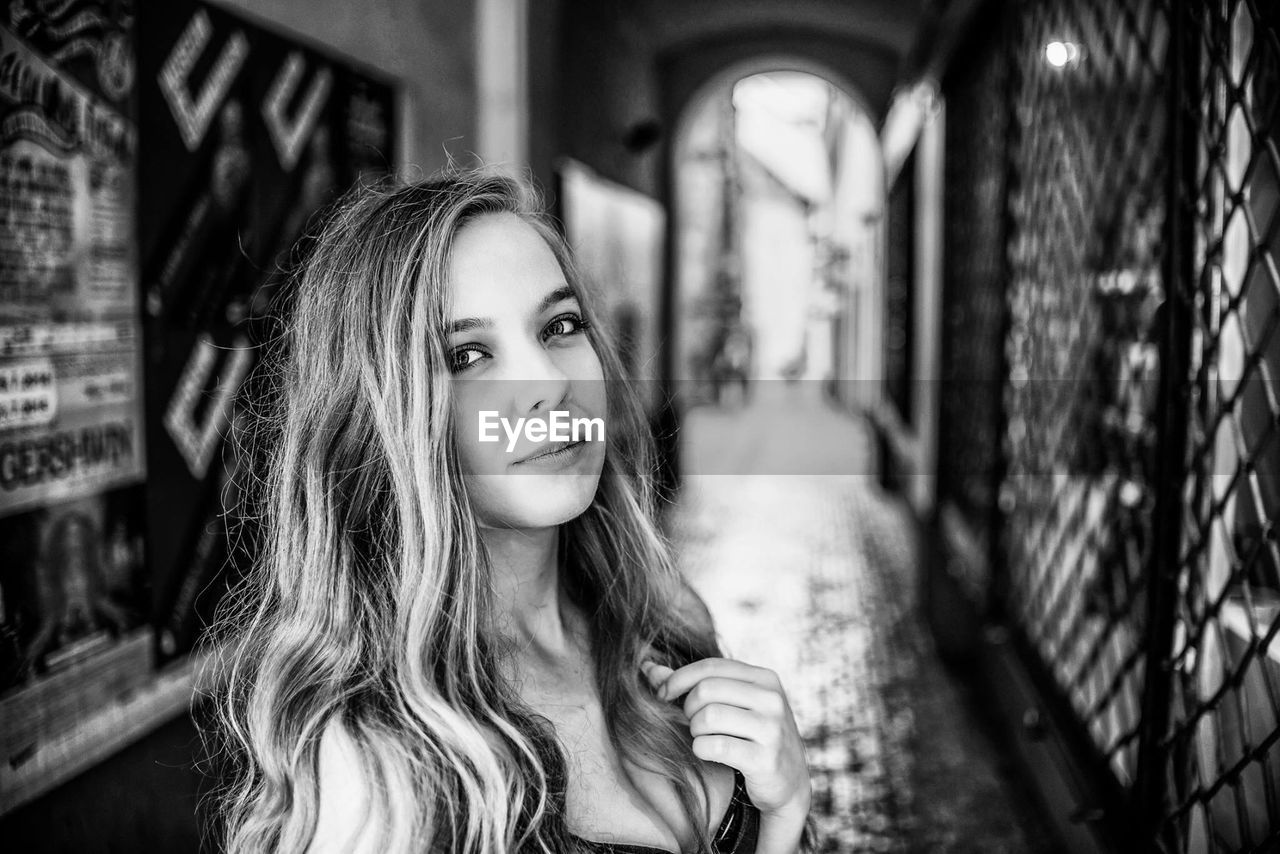 Portrait of smiling young woman standing in aisle of buildings