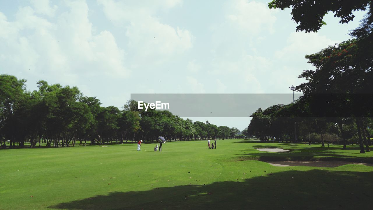 People on golf course against sky