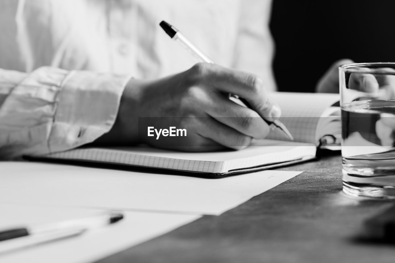 Midsection of man writing on book at table