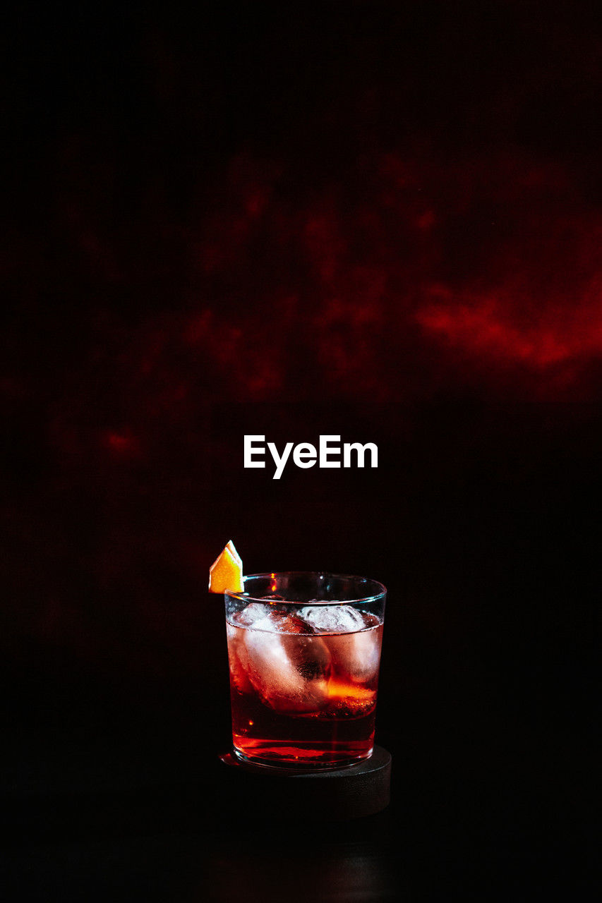 Close up of negroni cocktail in tumbler glass with dark red nebula background