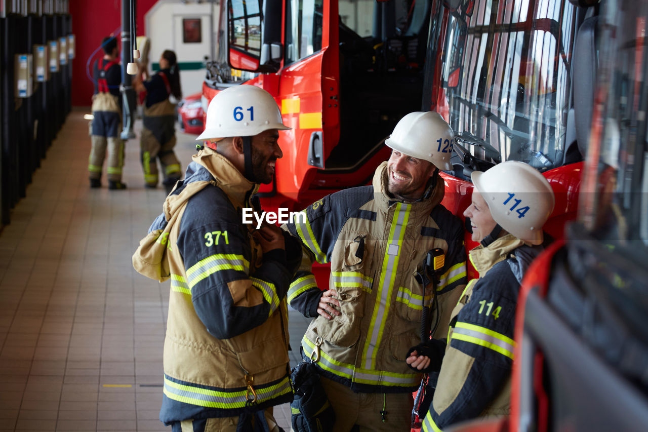 Coworkers smiling while standing against fire engine at fire station