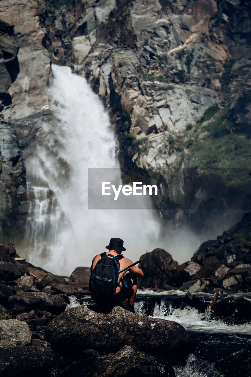 Man surfing on rocks against waterfall