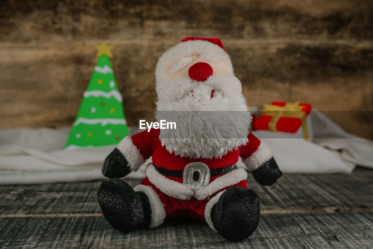 Santa doll on a wooden floor with a christmas tree  and two gift boxes