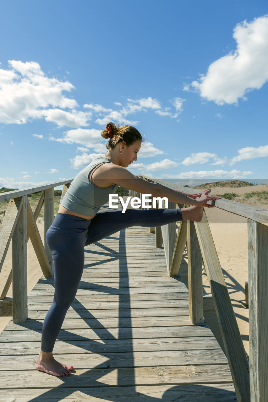 Woman performing pilates-yoga on wooden walkway next to the beach