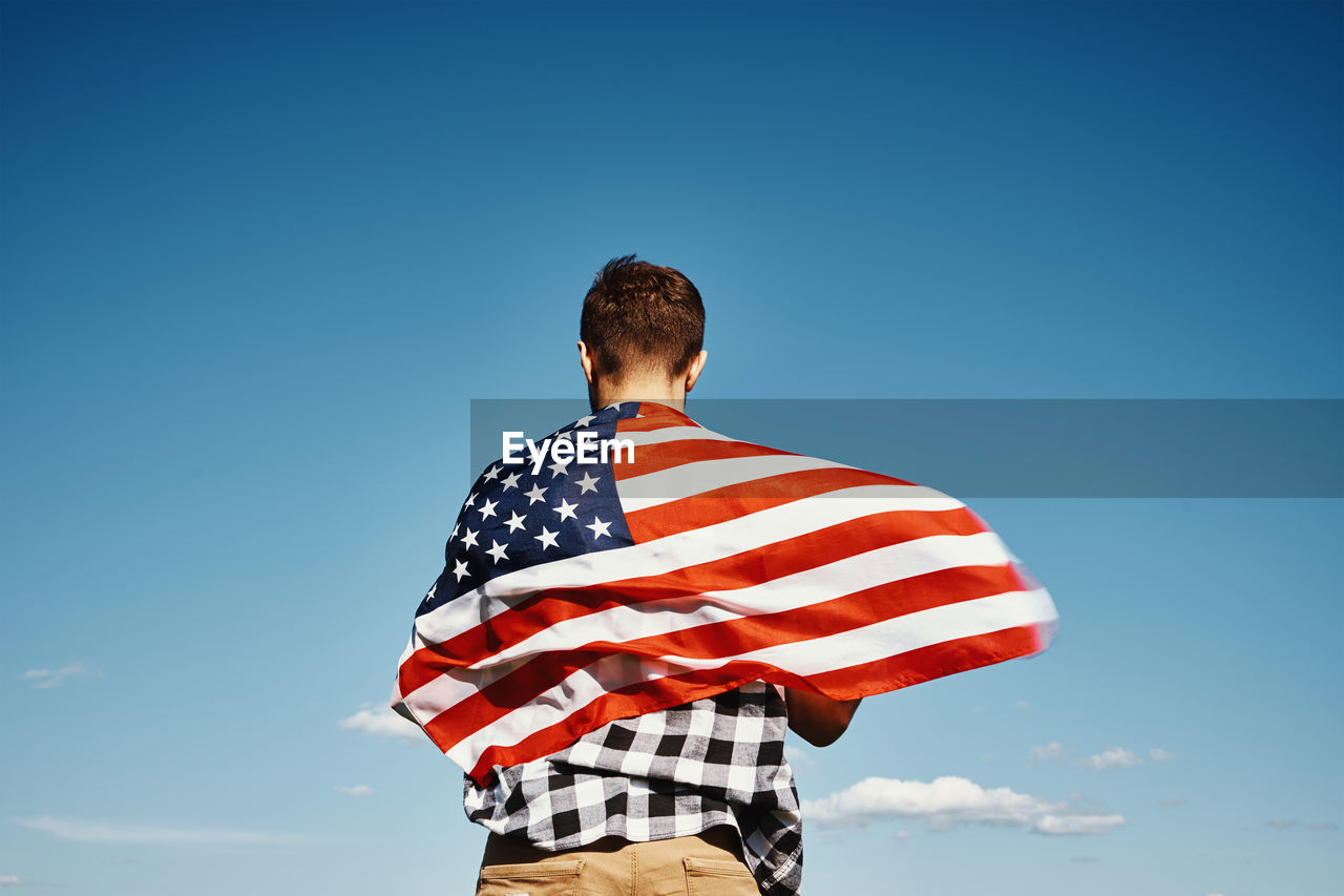 American flag outdoors. man holds usa national flag against blue cloudy sky. 4th july