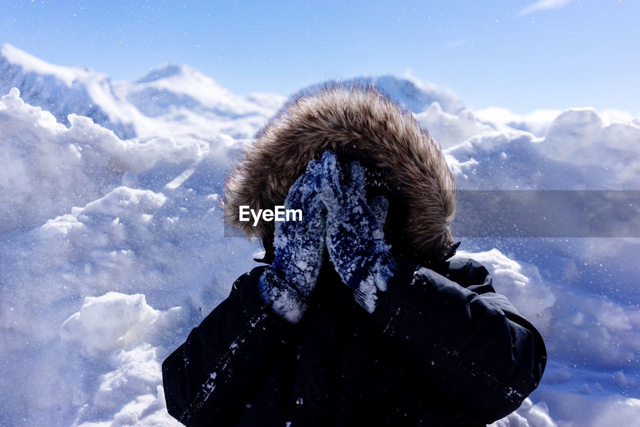 Boy in warm clothing covering face with hands