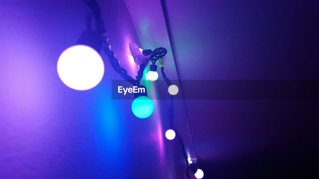 Low angle view of illuminated lighting equipment hanging against wall