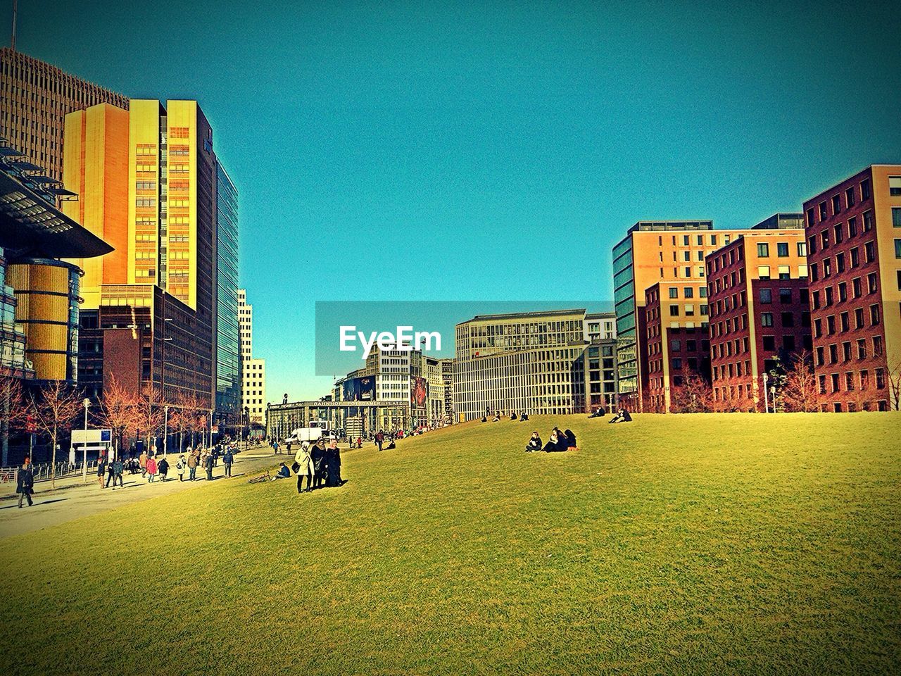 People of grassy field in city against clear blue sky at potsdamer platz