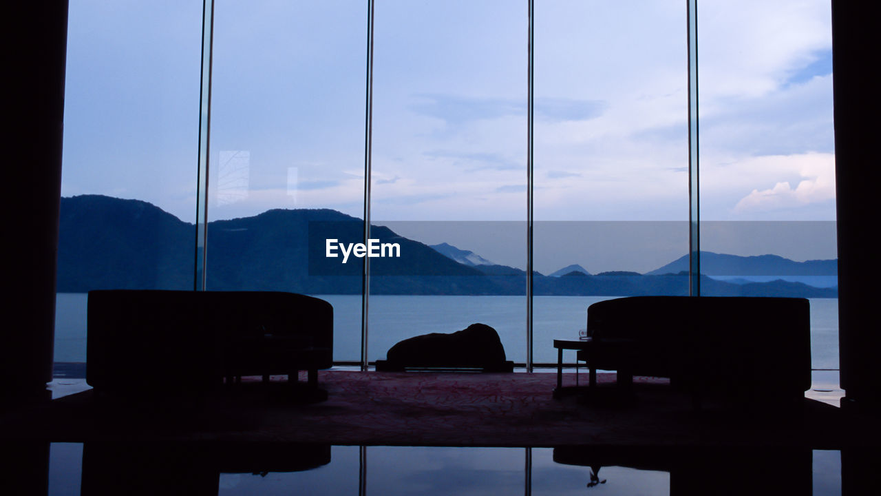 SILHOUETTE CHAIRS AND TABLE AGAINST SKY SEEN THROUGH WINDOW