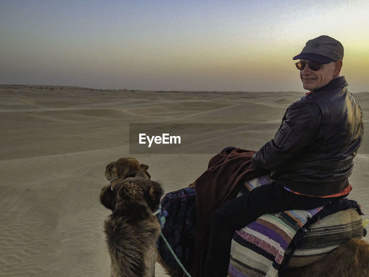 Man on dromedary in the sahara against sky