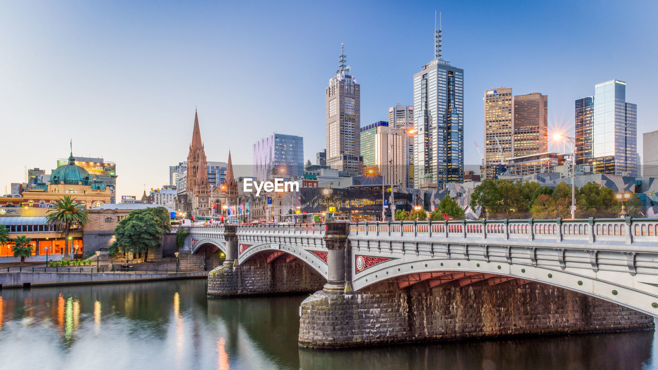 Modern buildings in front of yarra river against clear sky at dusk