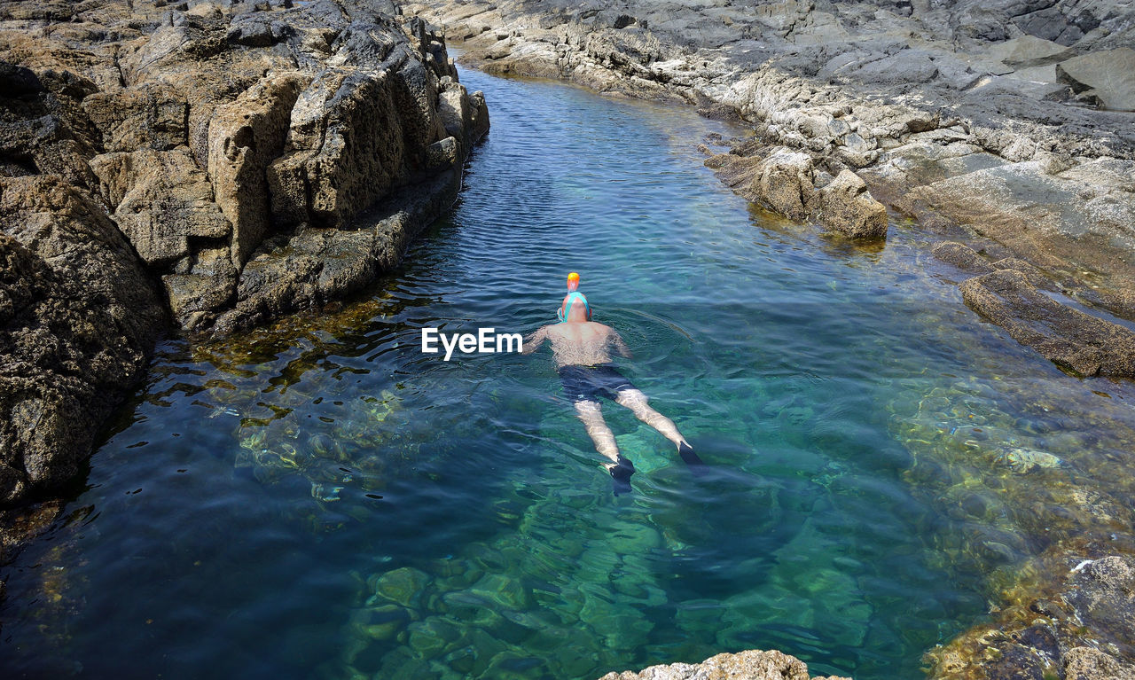 REAR VIEW OF PERSON SWIMMING ON ROCK